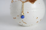 Gold necklace with a lapis lazuli pendant on a textured white surface