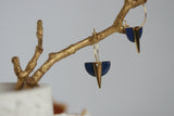 Navy blue earrings with gold accents hanging from a branch against a neutral background