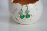 Green earrings hanging from a ceramic bowl with gold interior