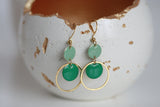 Green earrings with gold loops on a textured white and gold surface